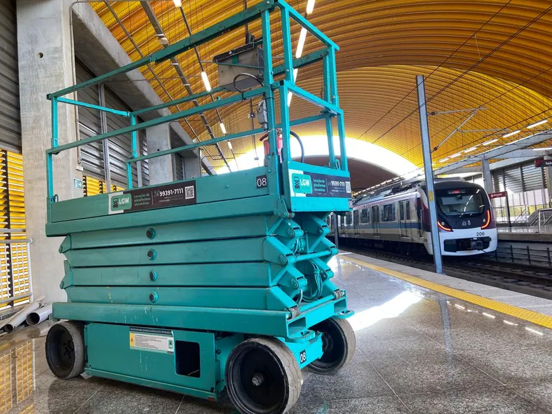 Plataforma tesoura verde-água dentro de uma estação de metrô, com o trem ao fundo