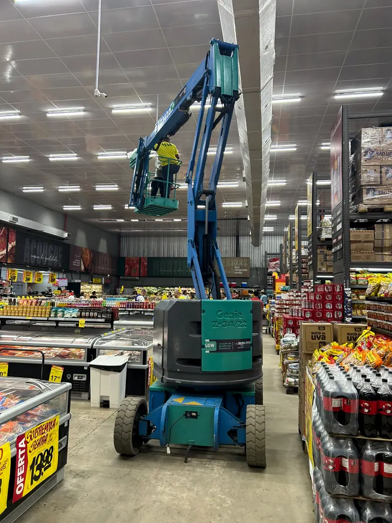 Plataforma articulada azul com um operador no alto, dentro de um supermercado